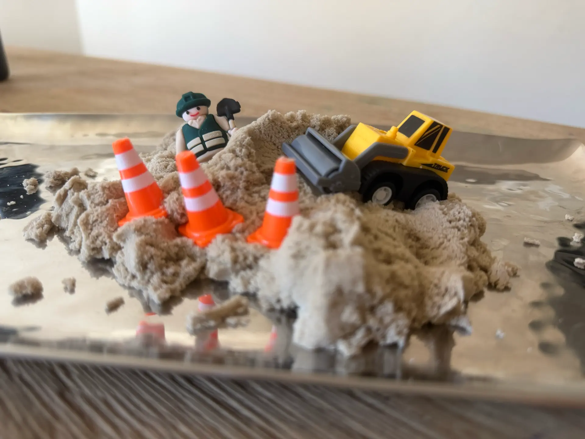 A construction-themed Mini Party Magic play scene with kinetic sand, a yellow loader, traffic cones, and a worker figure